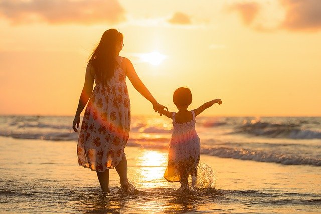 Matka z dzieckiem na plaży idące pod rękę o zachodzie słońca